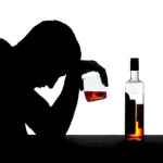 photo of a silhouette of a man holding a glass half full of liquor up to his head and a half empty bottle on the table beside him - alcoholism signs and symptoms - breakaway hired power