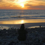 photo of a silhouette sitting on the beach watching the sunset over the ocean - breakaway