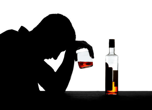 photo of a silhouette of a man holding a glass half full of liquor up to his head and a half empty bottle on the table beside him - alcoholism signs and symptoms - hired power breakaway