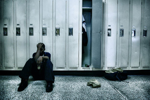 photo of a teenage boy sitting on the ground in front of his locker with his head in his hands - long term drug rehab essential for teens - breakaway hired power